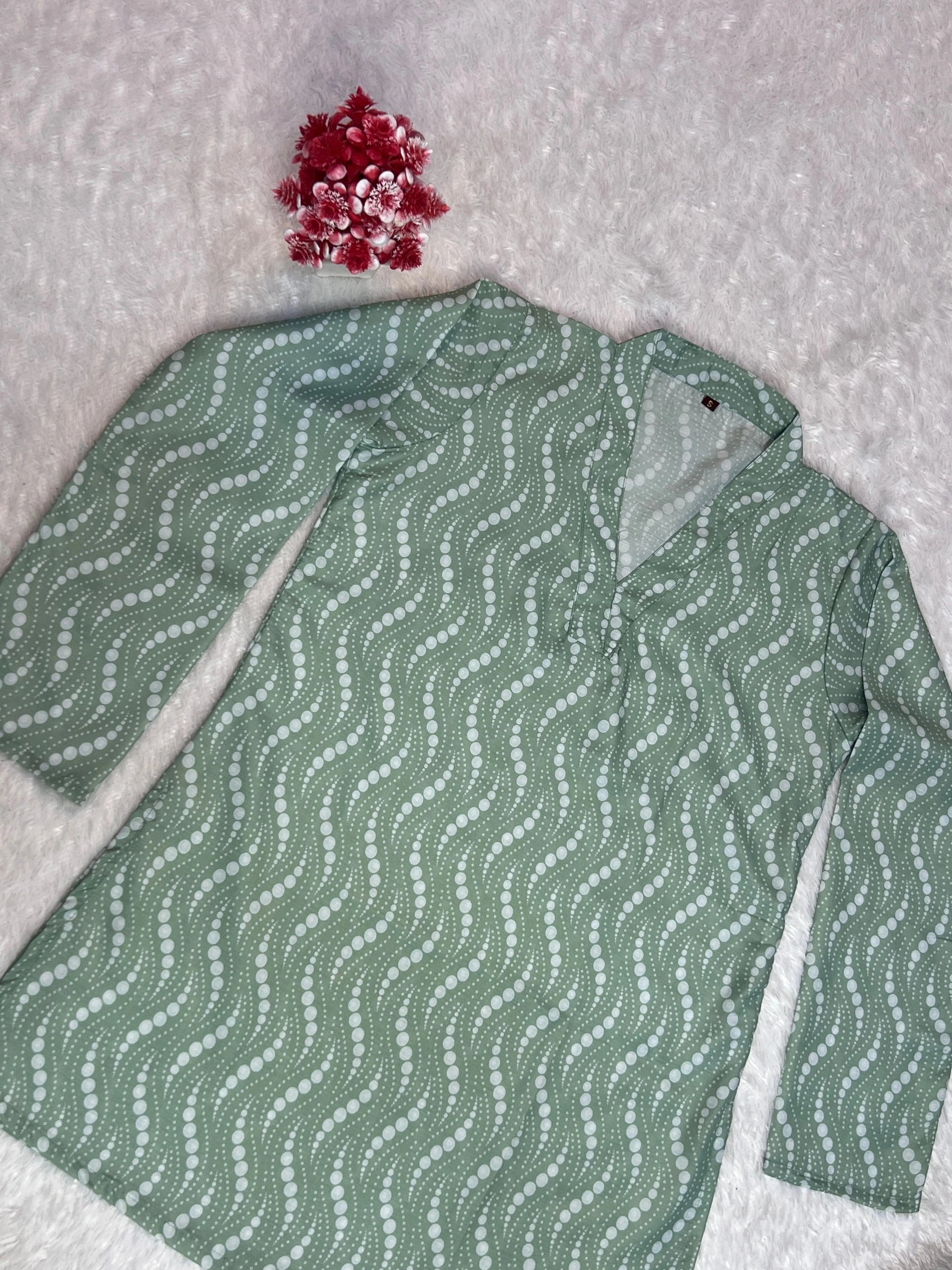 Green patterned shirt on a textured surface with red flowers.