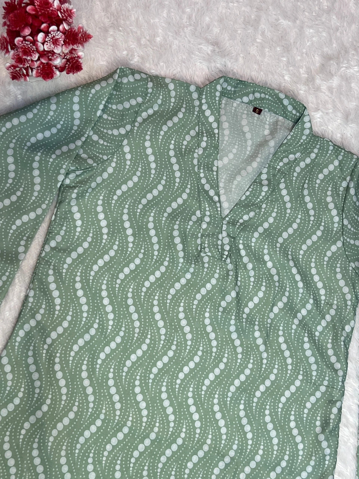 Green patterned shirt on a textured surface with red flowers in the corner