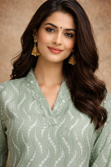 Woman wearing a light green traditional outfit with gold jewelry against a beige background