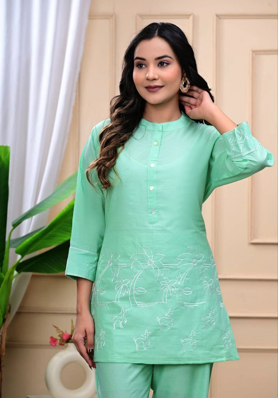Woman wearing a light green traditional outfit with embroidery, standing indoors.