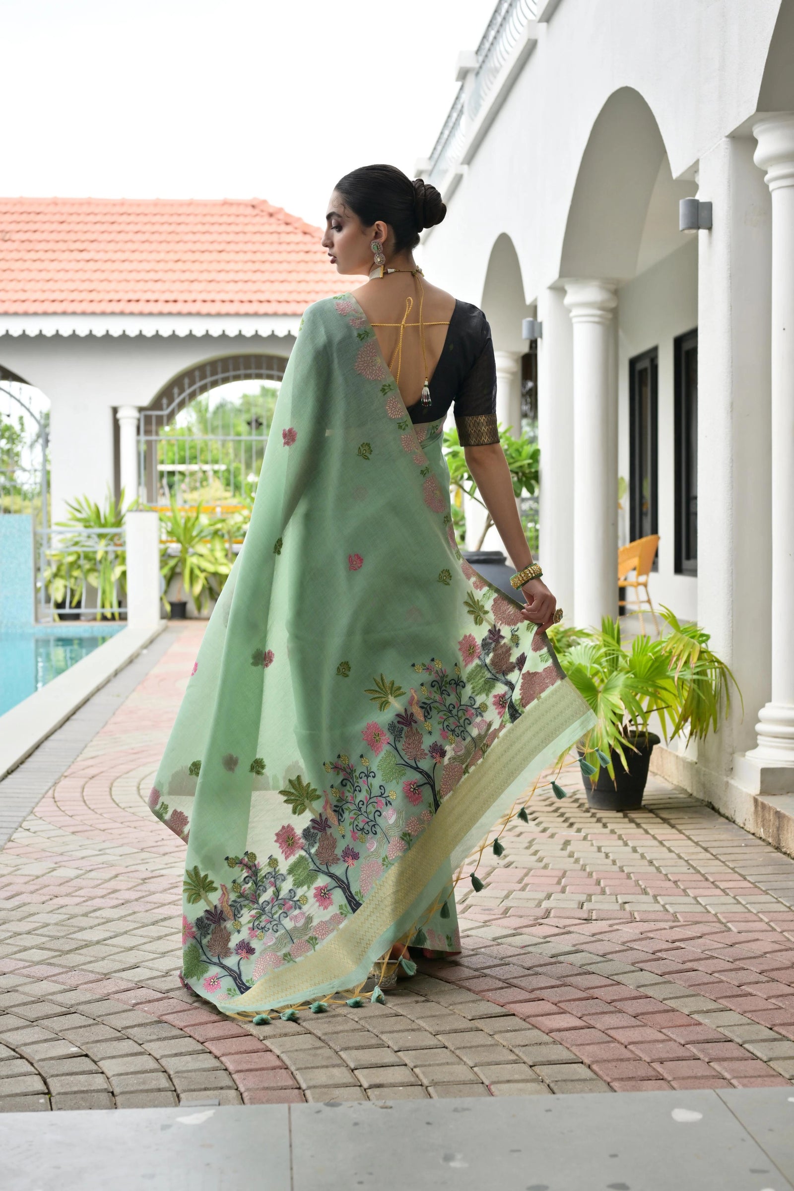 Woman in a light green saree with floral patterns walking near a poolside.