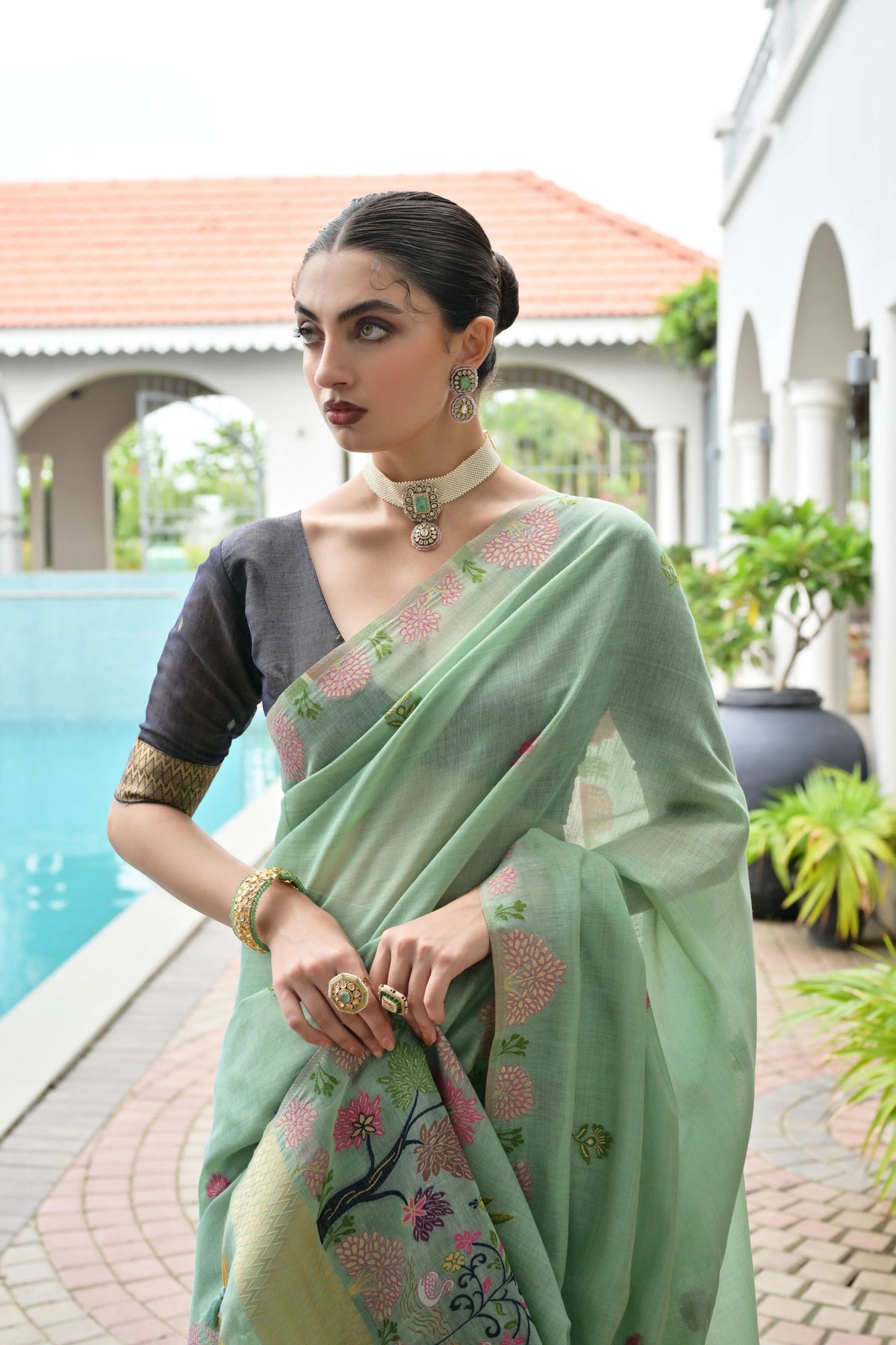 Woman in a light green saree with floral patterns standing by a poolside.