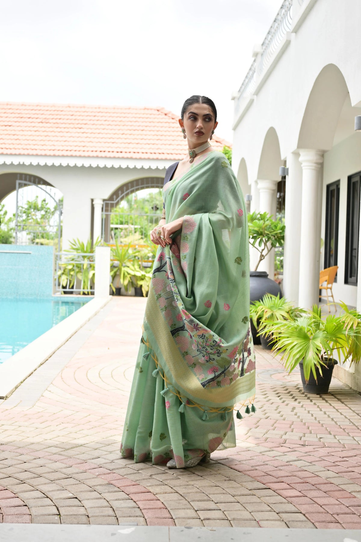 Woman in a light green saree with a floral pattern standing by a poolside.