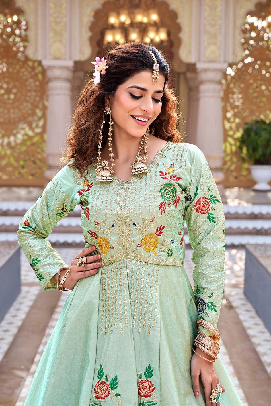 Woman in a light green embroidered traditional outfit standing in an ornate indoor setting.