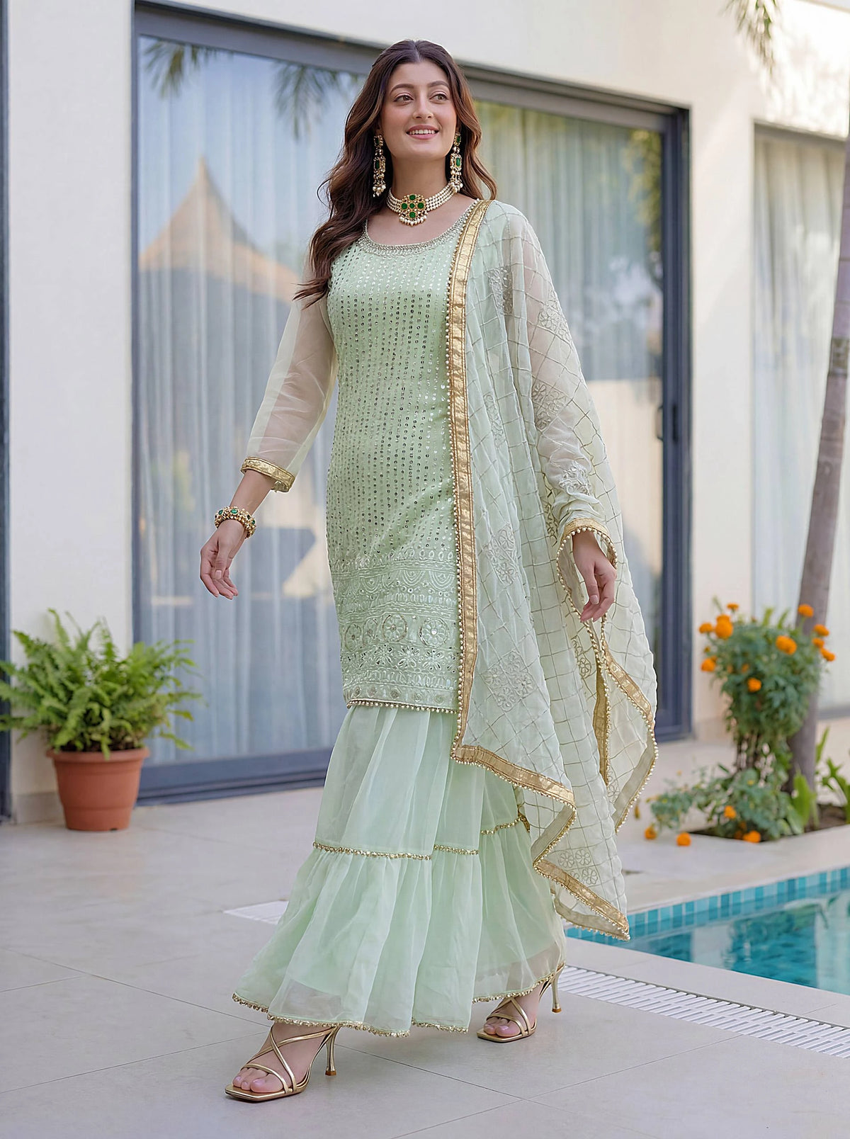 Woman in a light green traditional outfit standing by a poolside.
