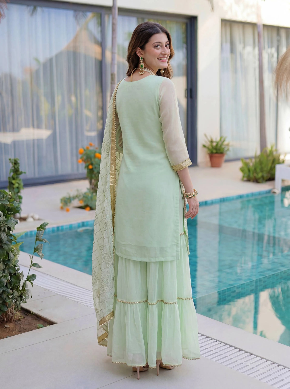 Woman in a light green traditional outfit standing by a pool