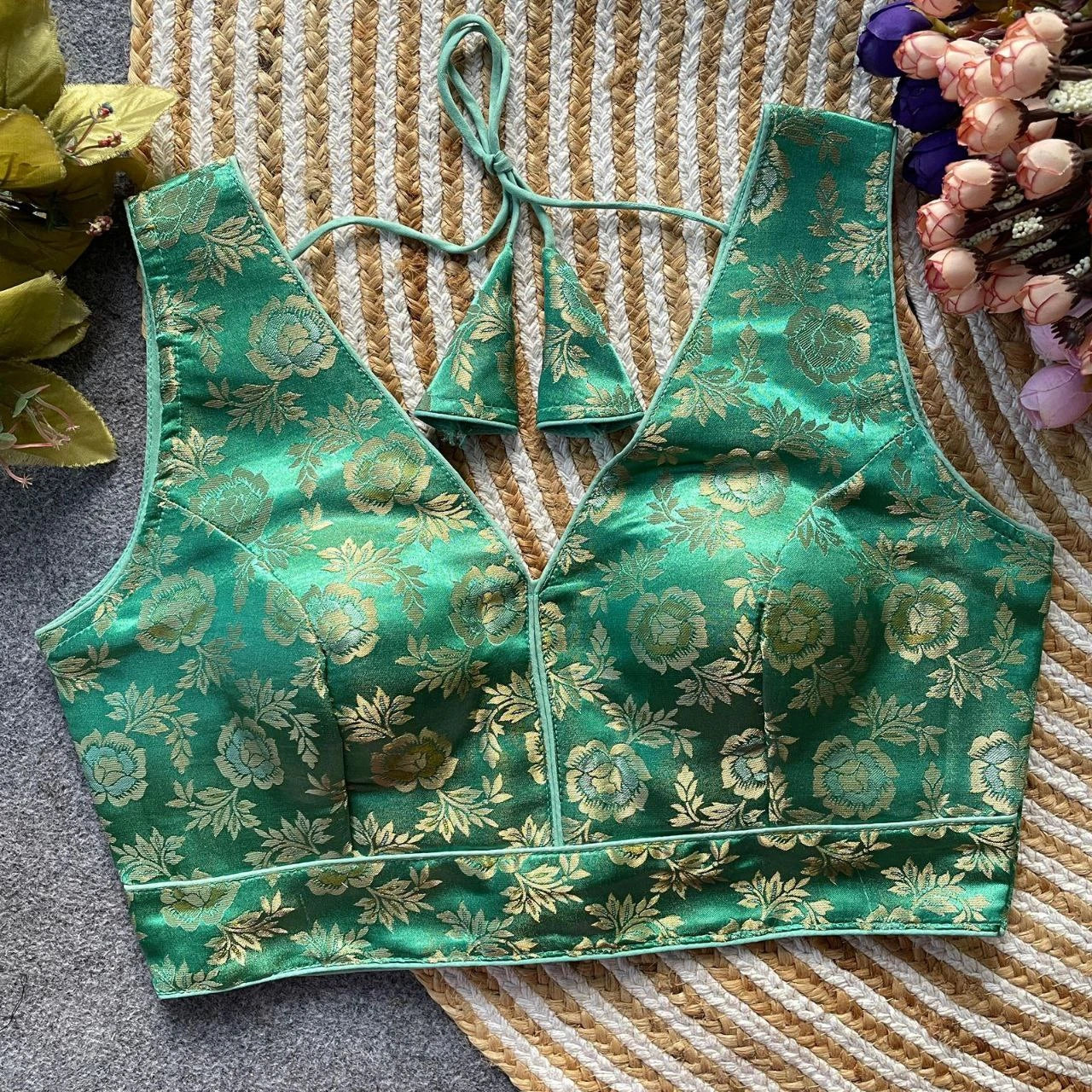 Green floral-patterned top on a textured surface with flowers in the background