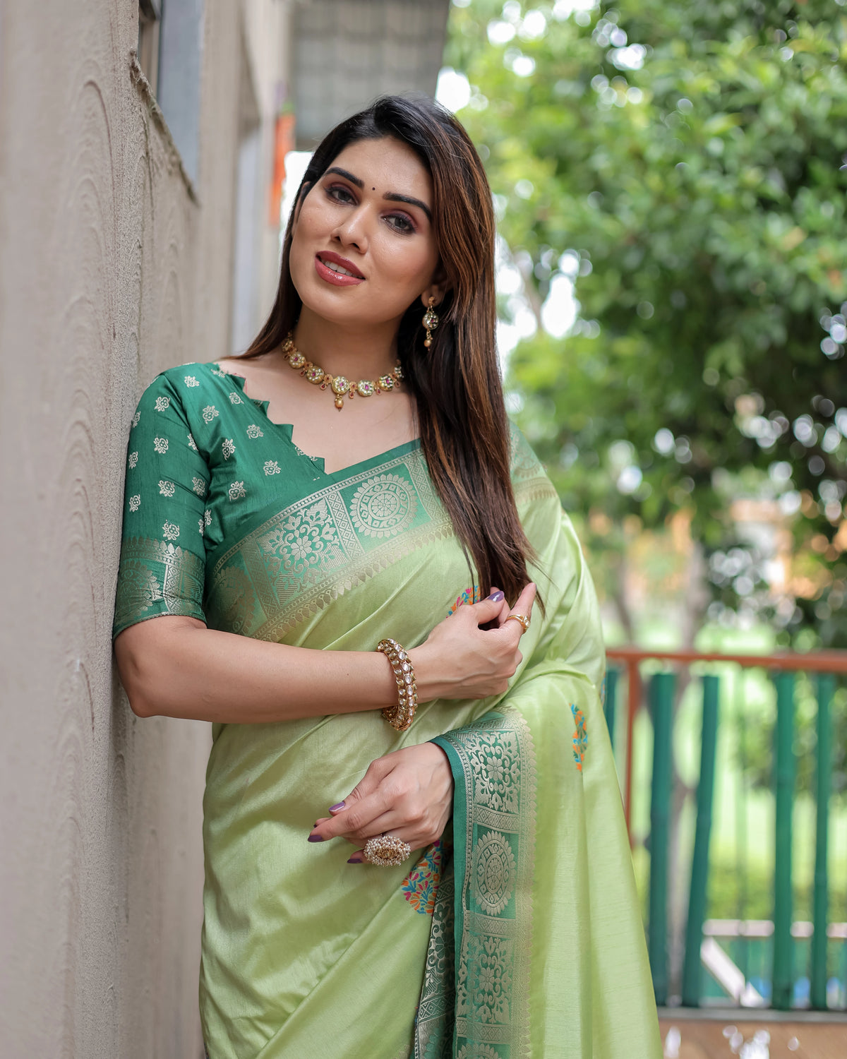 Woman wearing a green and light green saree with a blurred outdoor background