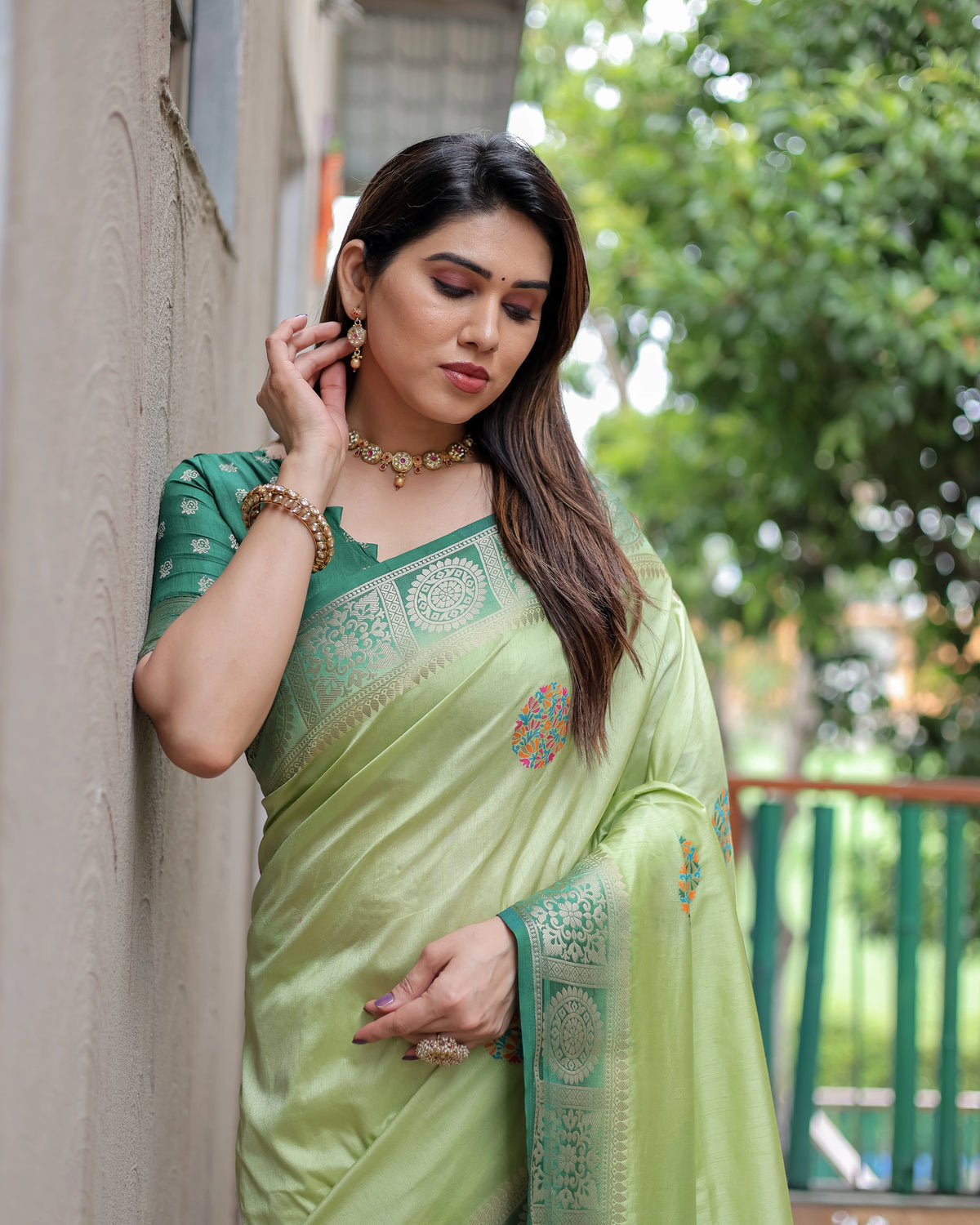 Woman wearing a green saree with a blurred outdoor background