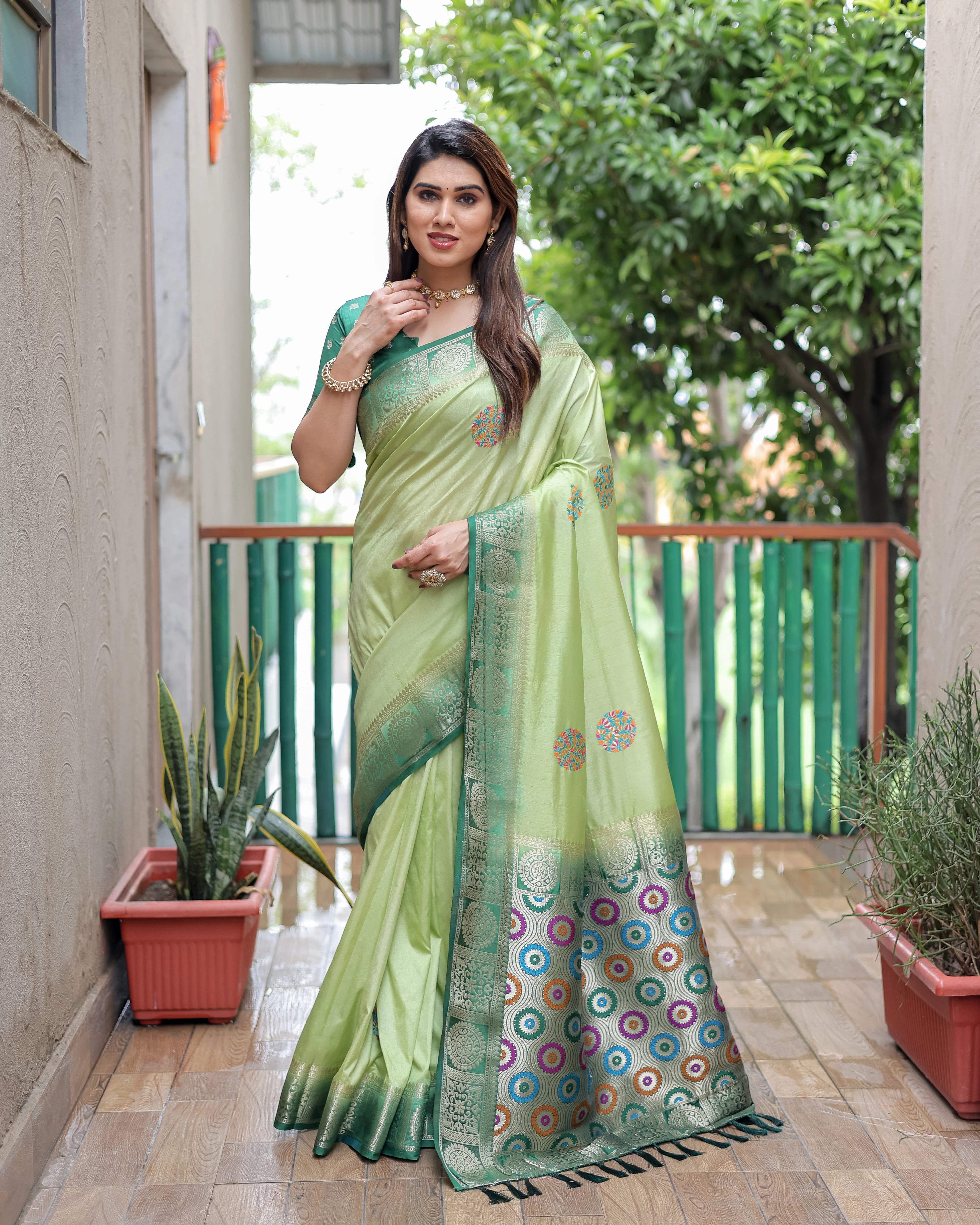 Woman wearing a green saree with a colorful border in an outdoor setting.