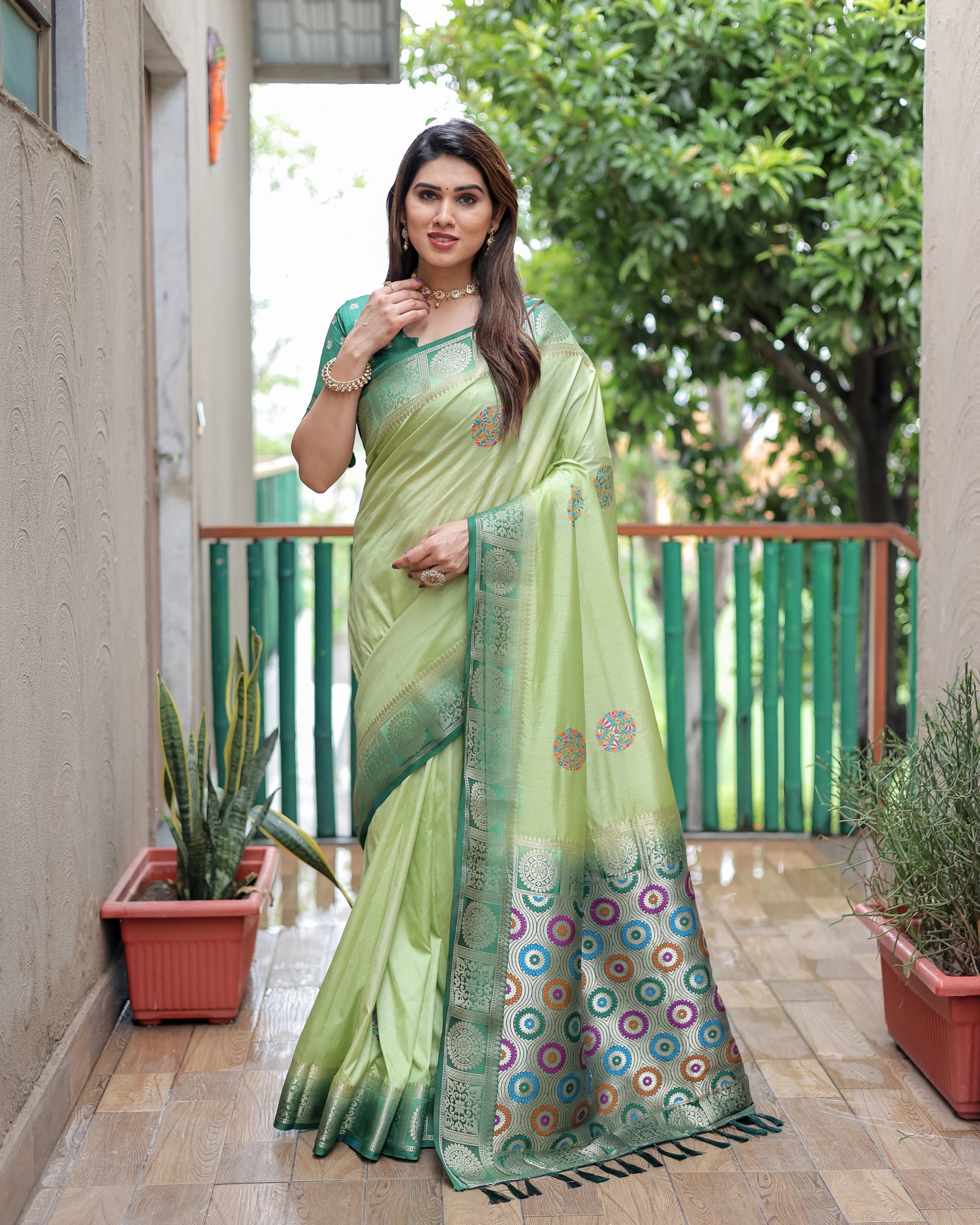 Woman wearing a green saree with a colorful border in an outdoor setting.