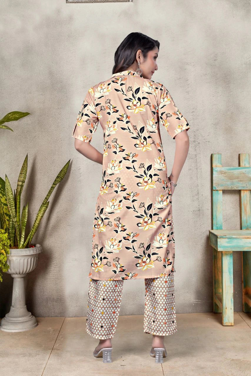 Woman wearing a floral kurta with pants in a room with a plant and wooden chair.