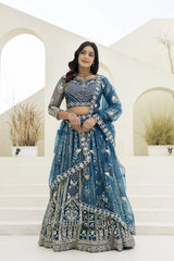 Woman in a blue embroidered traditional outfit standing in front of decorative arches.