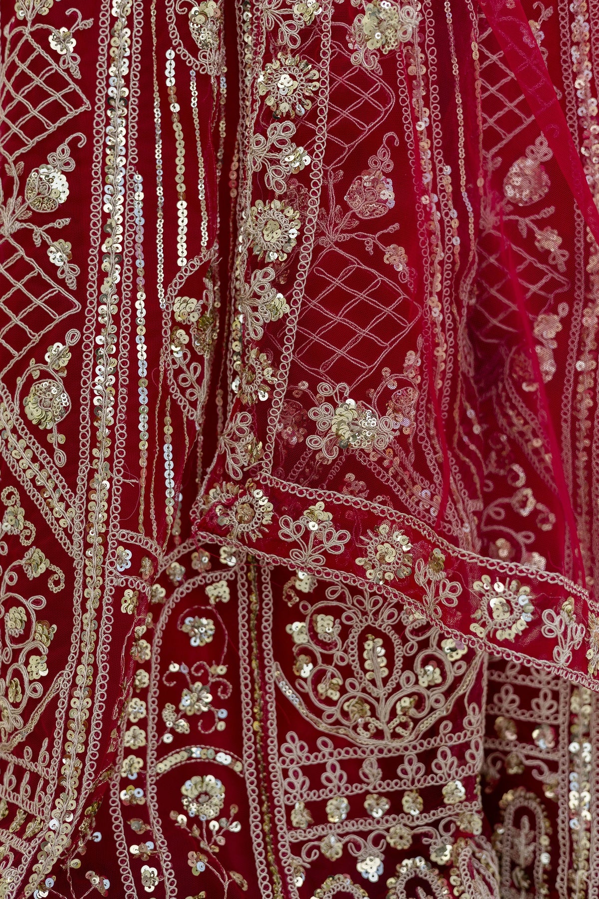 Close-up of a red fabric with intricate gold embroidery and sequin work.