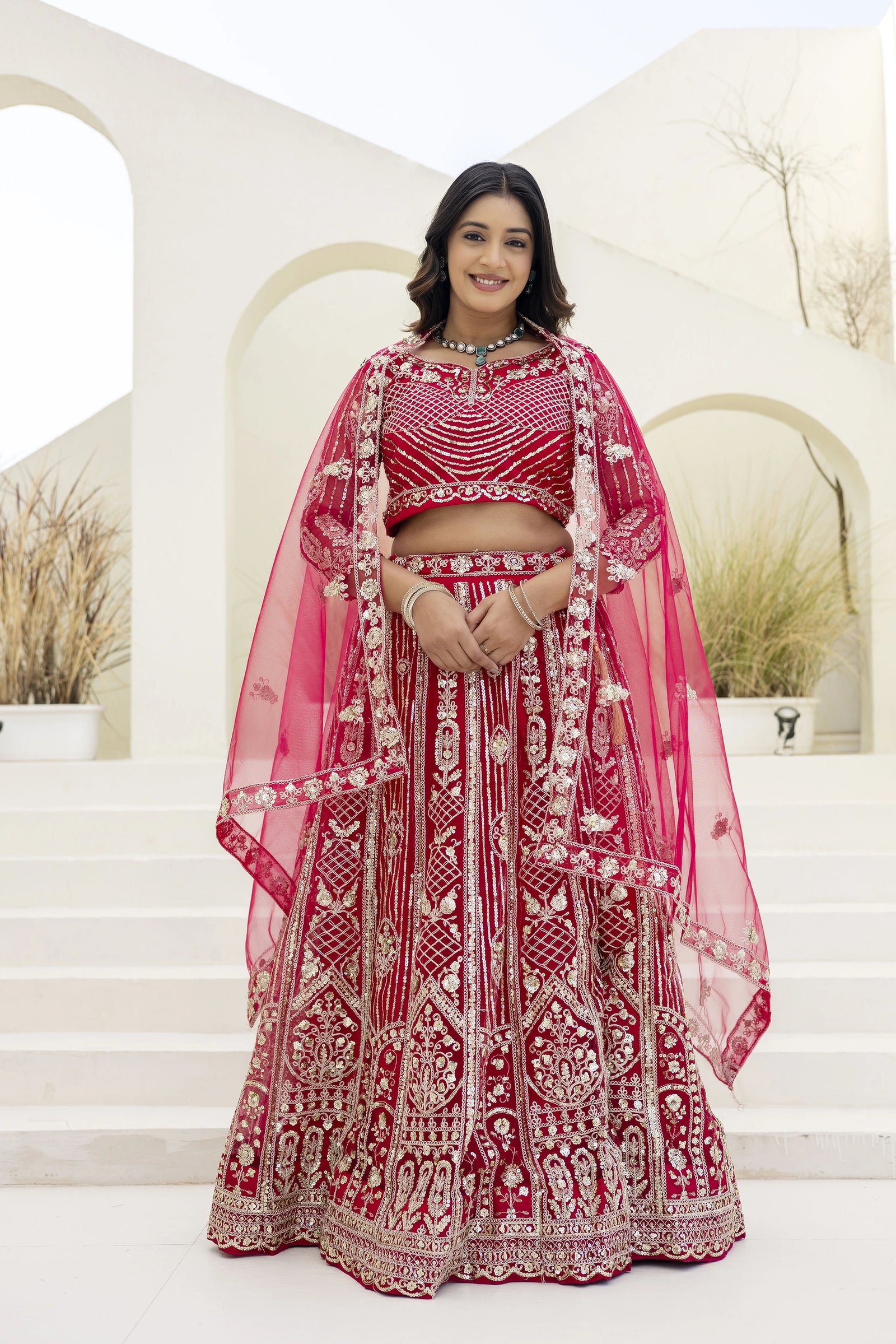 Woman in a red and white embroidered traditional outfit standing on steps with a neutral background