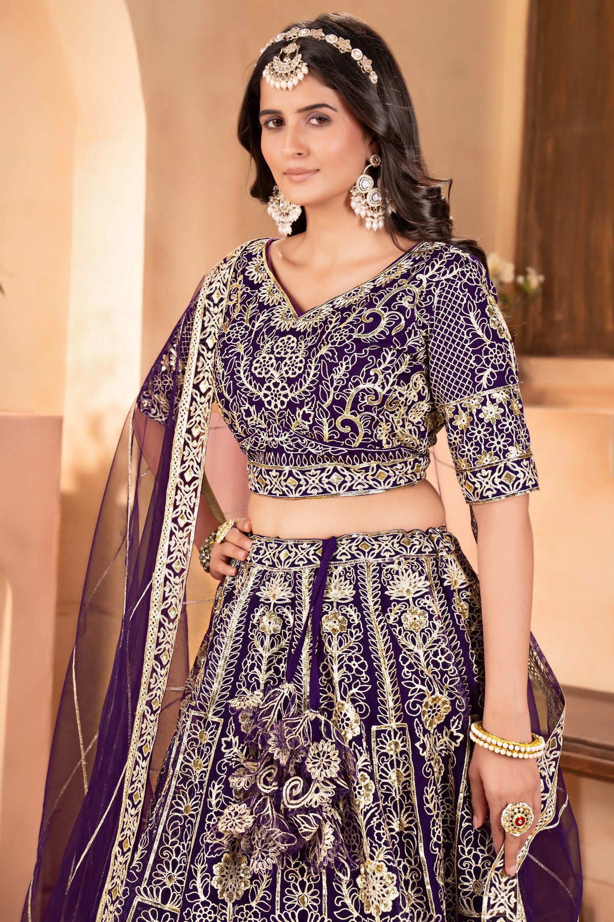 Woman wearing a traditional purple and gold embroidered outfit with jewelry.