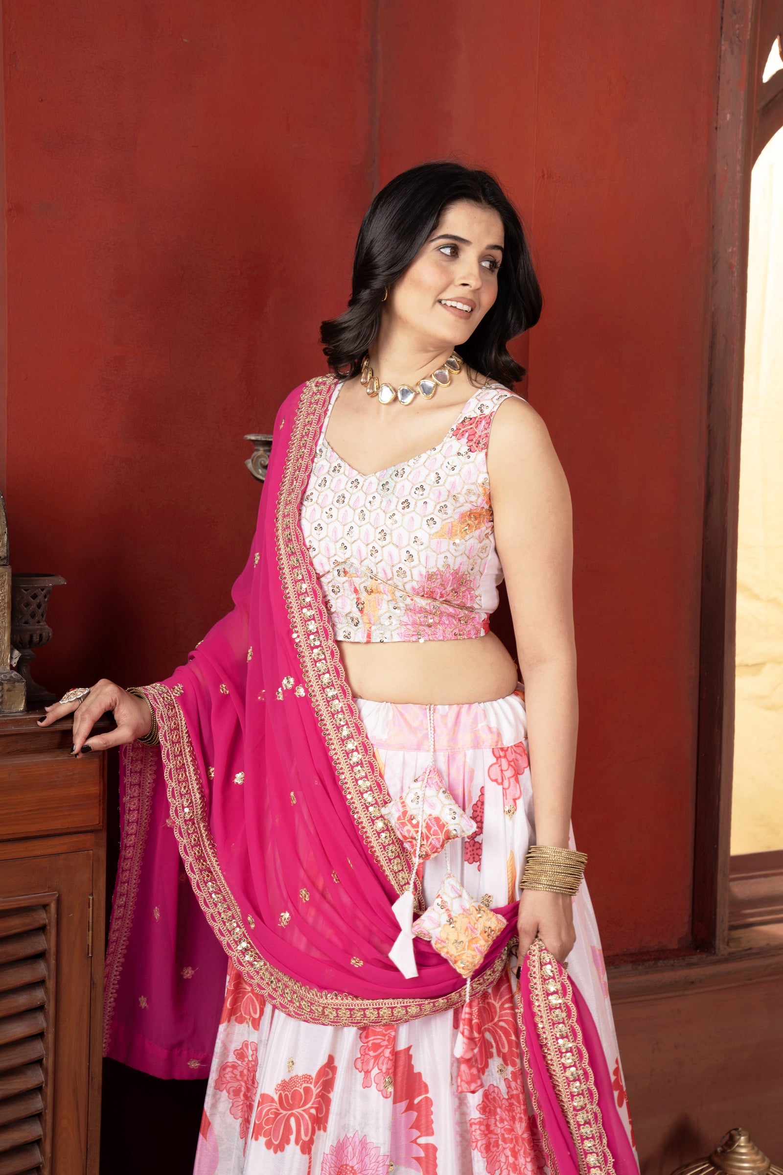 Woman in a traditional outfit with a pink and white saree against a red wall.