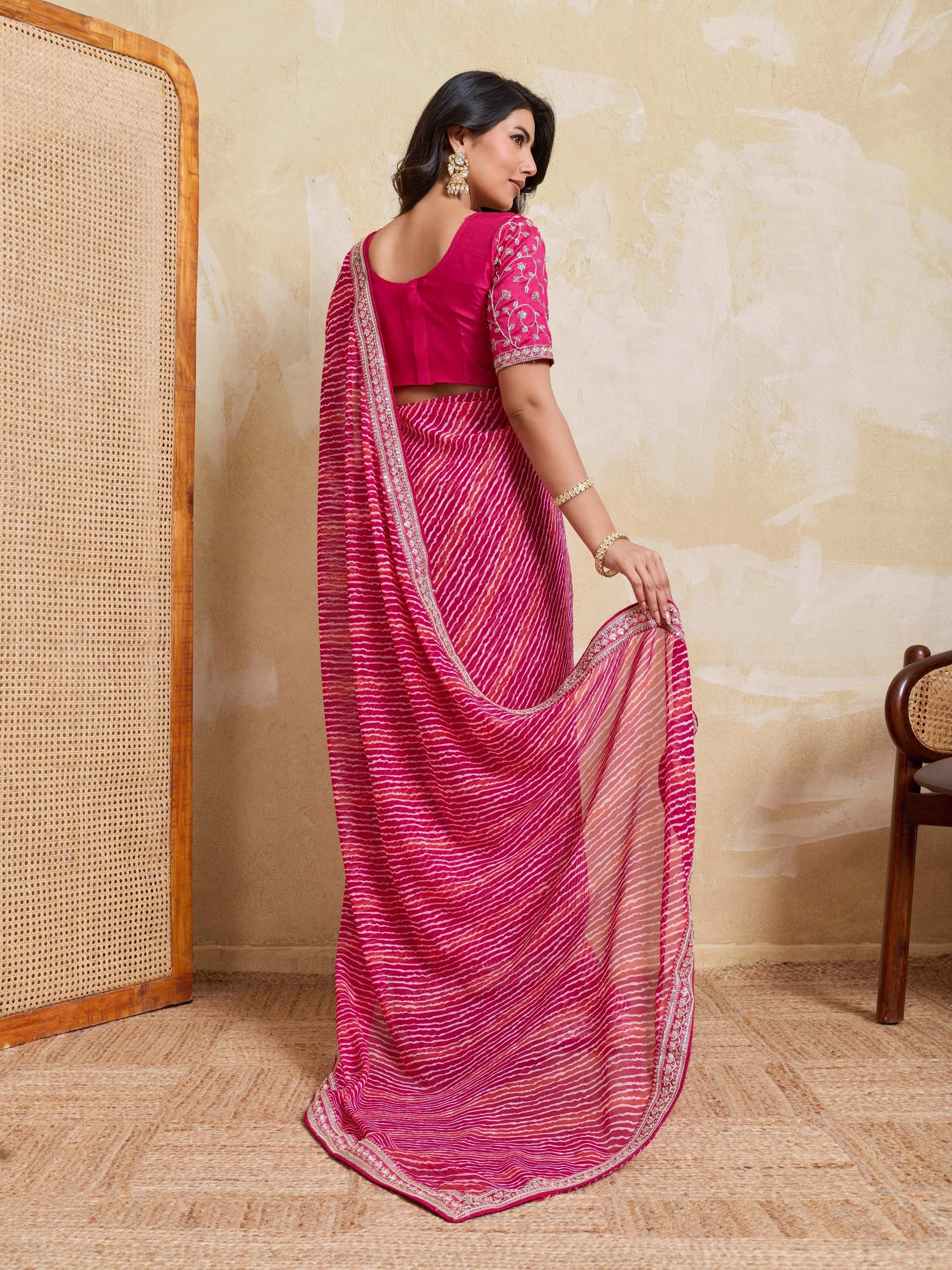 Woman wearing a pink saree with a matching blouse in a room setting.