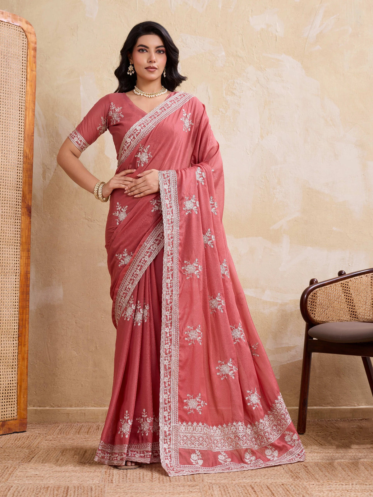 Woman wearing a pink saree with white embroidery against a beige wall.