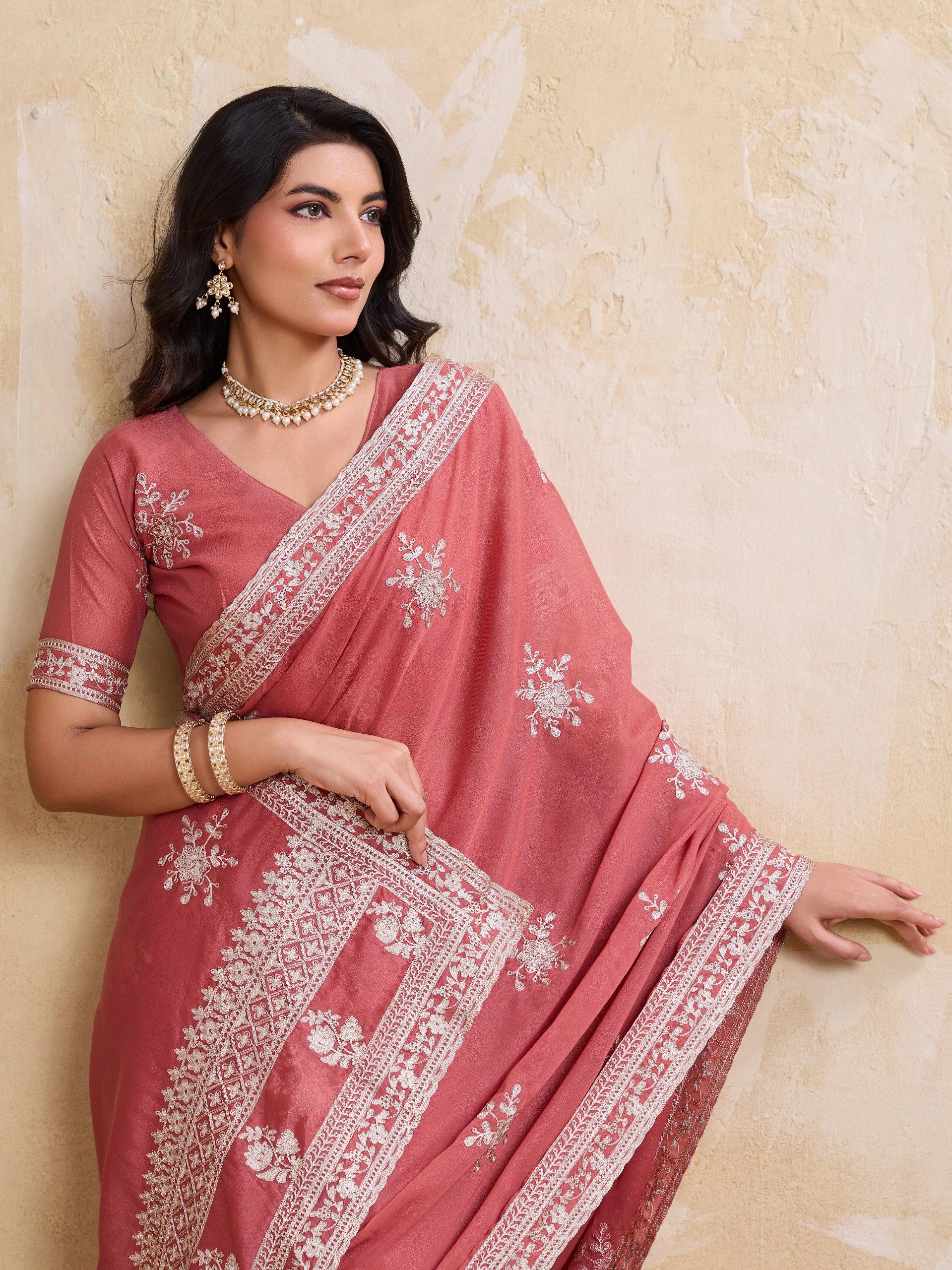Woman wearing a pink saree with white embroidery against a beige background