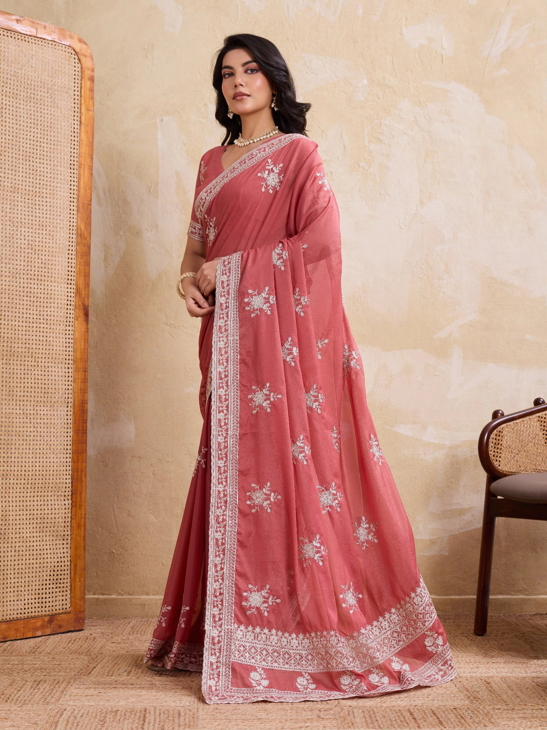 Woman wearing a pink saree with white patterns in a room setting.