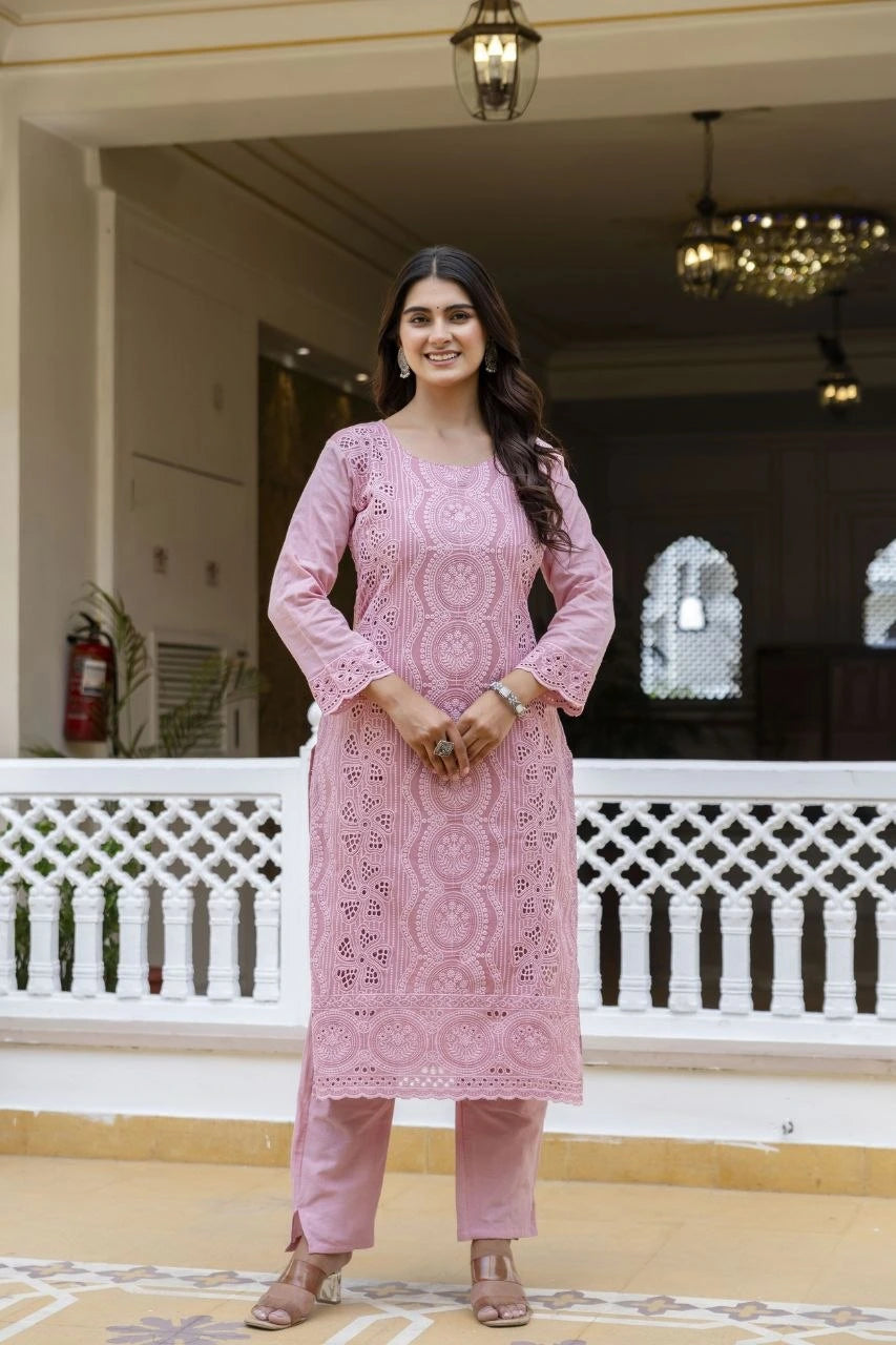 Woman in a pink traditional outfit standing in an indoor setting with white walls and decorative elements.