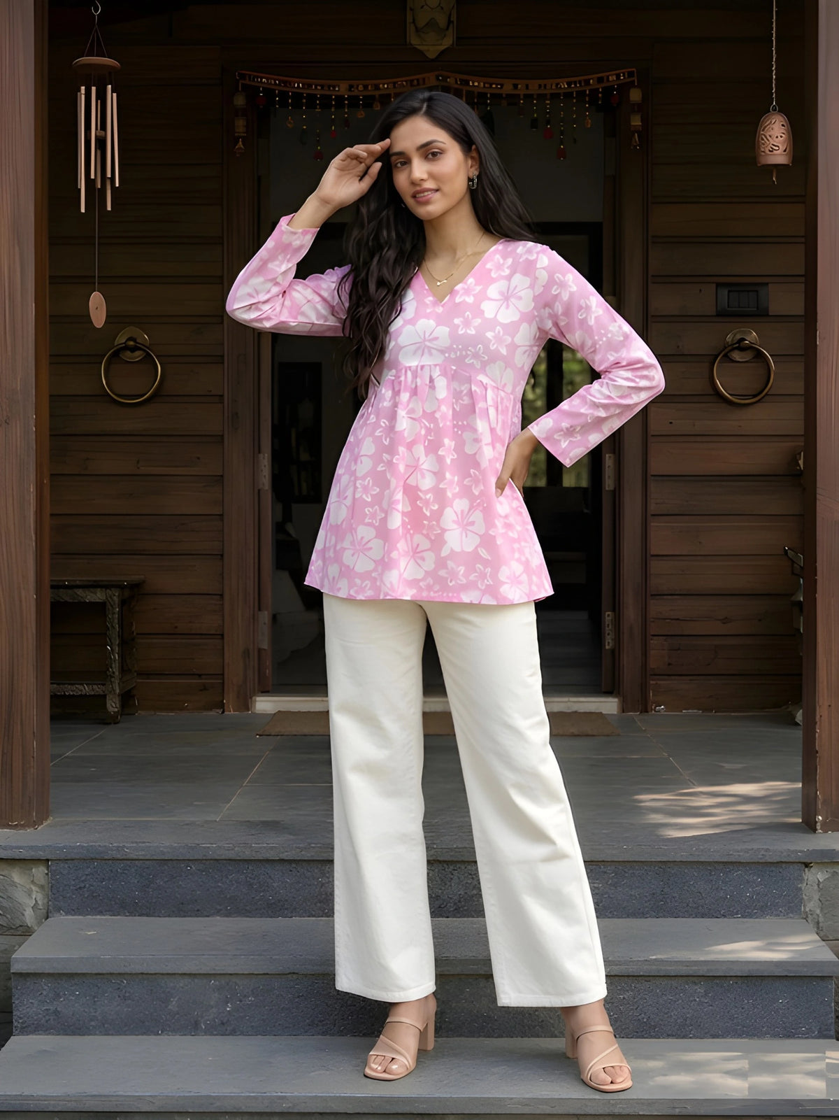 A full-length shot of a woman posing with one hand on her forehead and the other on her hip, wearing a pink floral outfit.