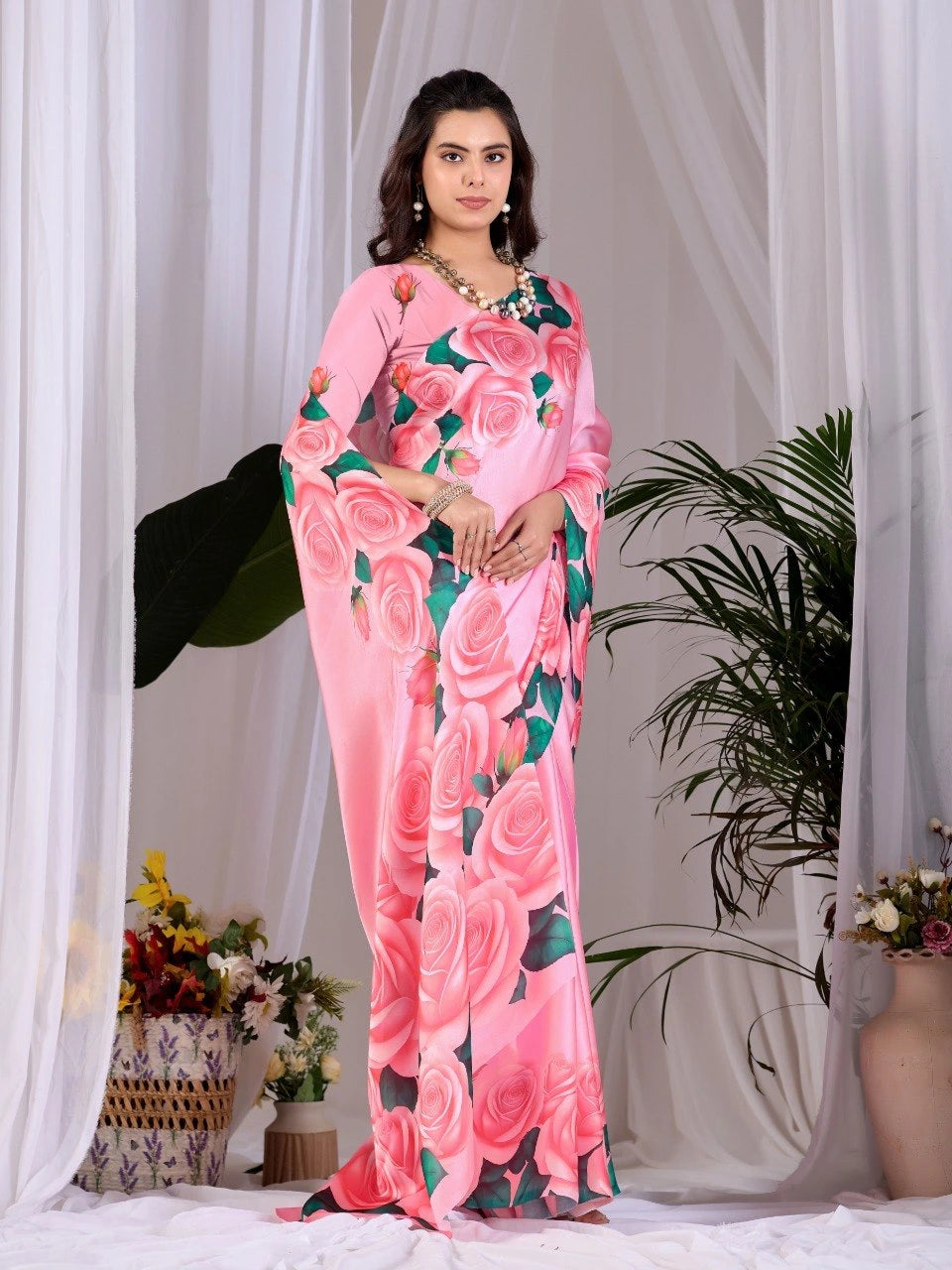 Woman wearing a pink floral saree with a white curtain and plants in the background