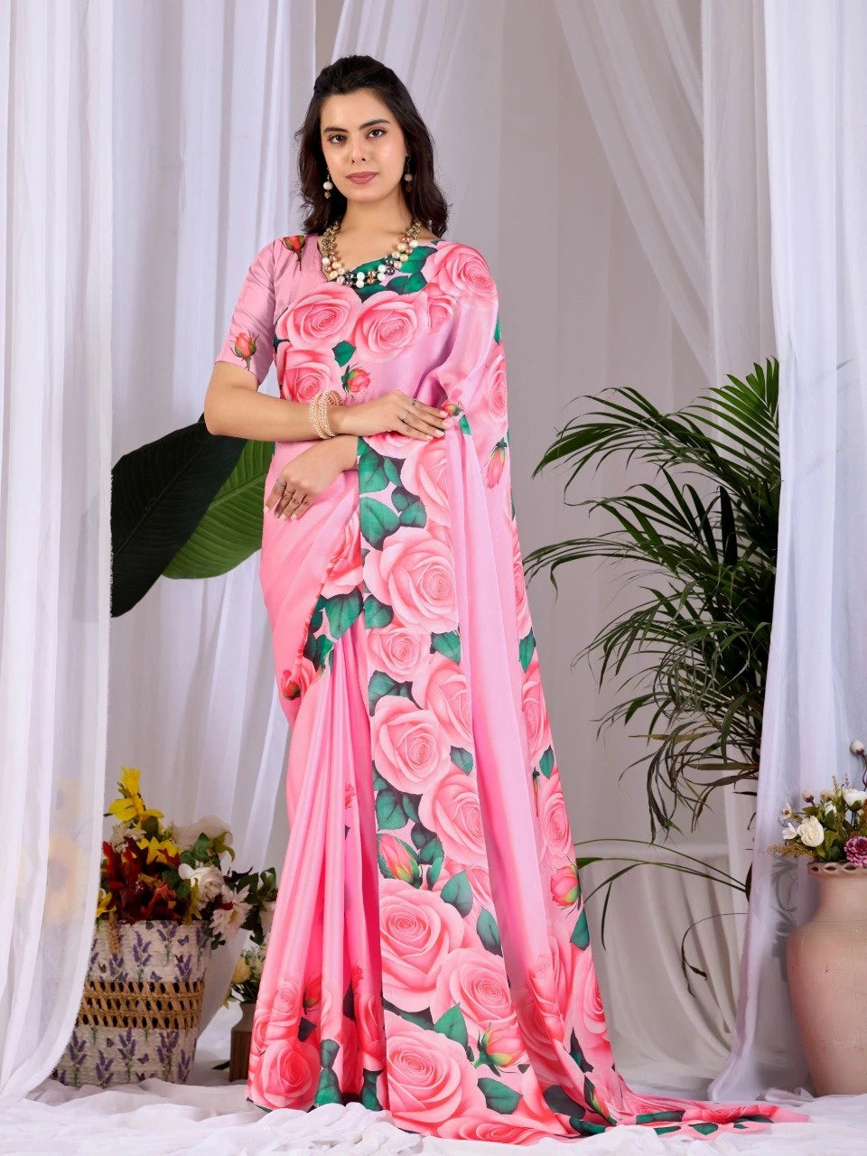Woman wearing a pink saree with floral patterns in a decorated indoor setting.