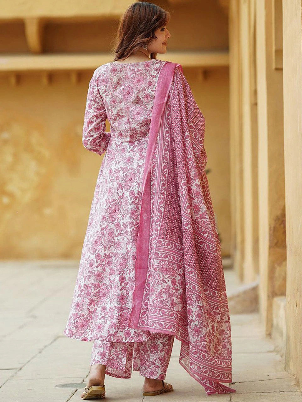 Woman wearing a pink and white traditional outfit with a matching dupatta in front of a beige wall.