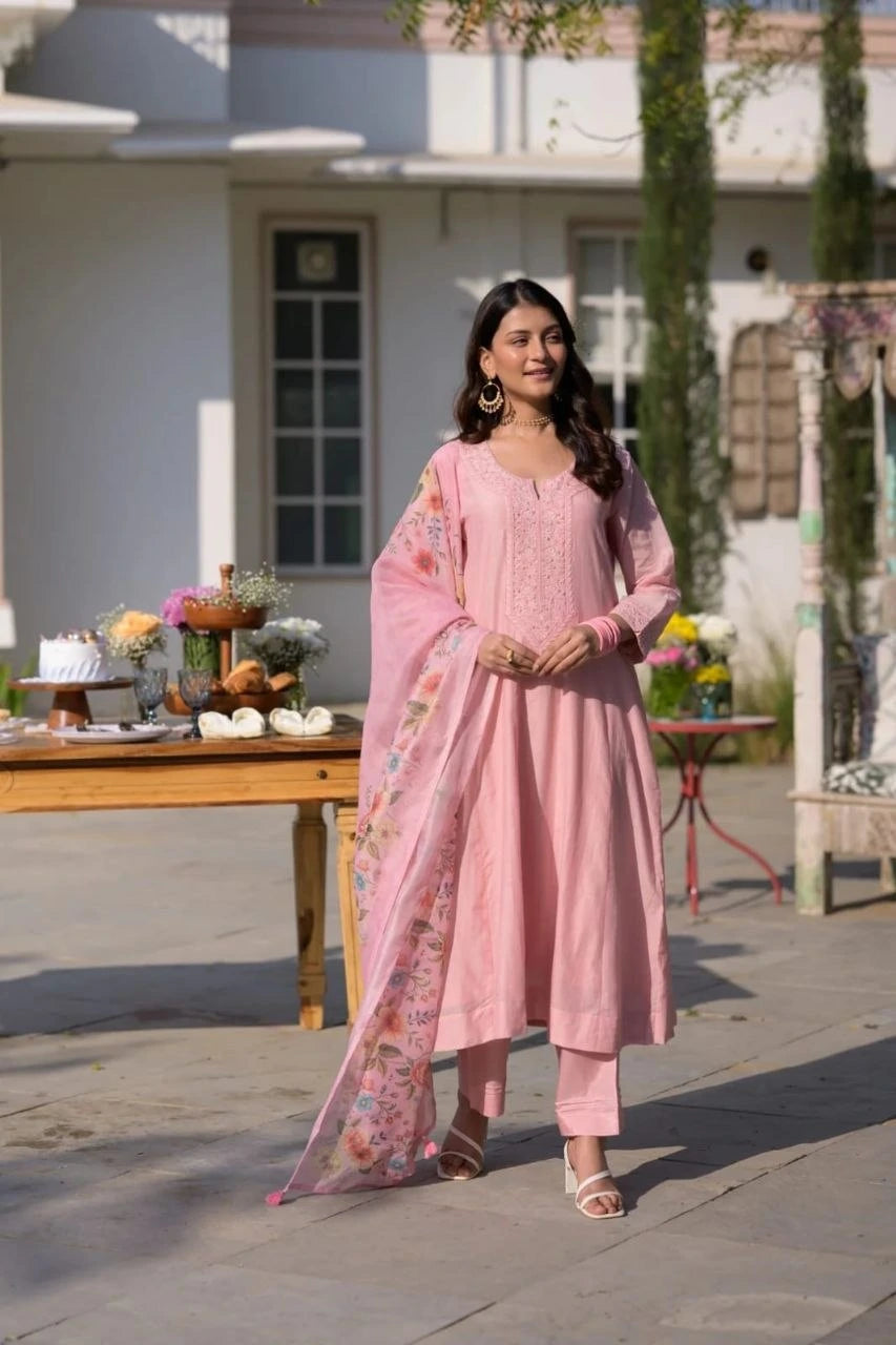 Woman in a pink traditional outfit standing outdoors with a table and plants in the background