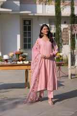 Woman in a pink traditional outfit standing outdoors with a table and plants in the background