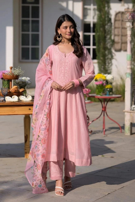 Woman in a pink traditional outfit standing outdoors with decorative elements.