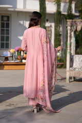 Woman in a pink traditional outfit standing outdoors with a building and garden in the background