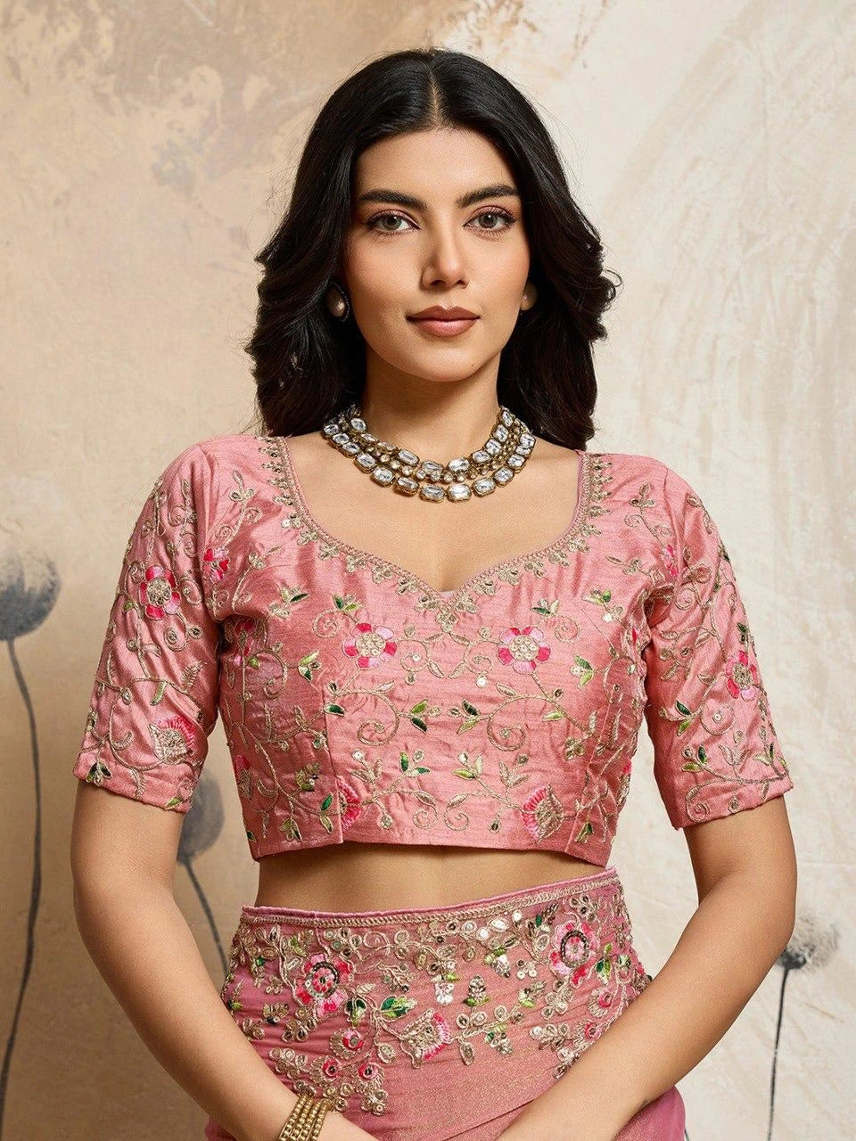 Woman wearing a pink embroidered traditional outfit with a neutral background