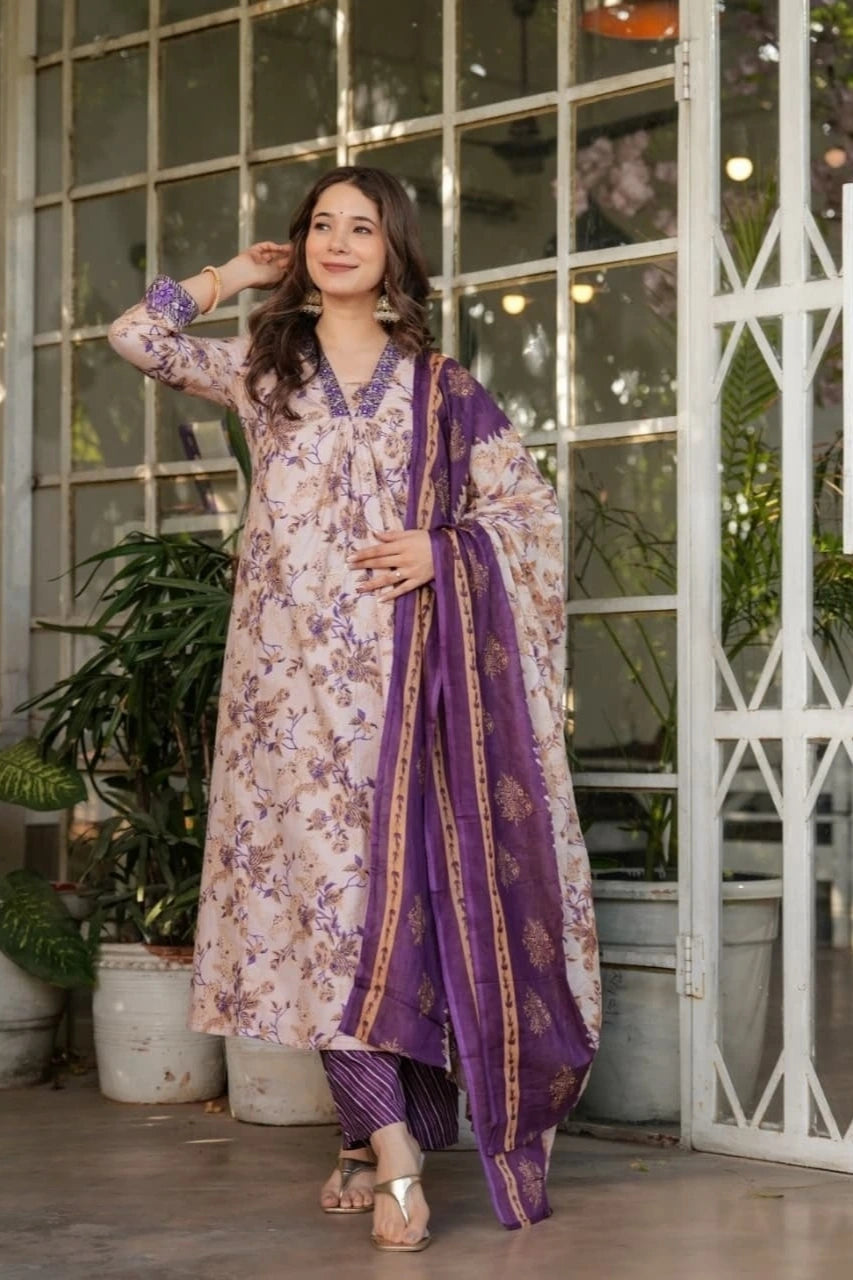 Woman in a floral dress with a purple dupatta standing in front of a glass door.