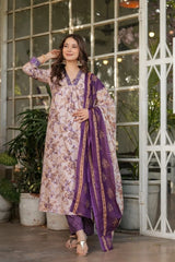 Woman in a floral dress with a purple dupatta standing in front of a glass door.