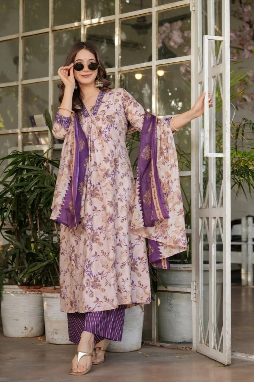 Woman in a floral dress with purple accents standing in a decorative indoor setting.