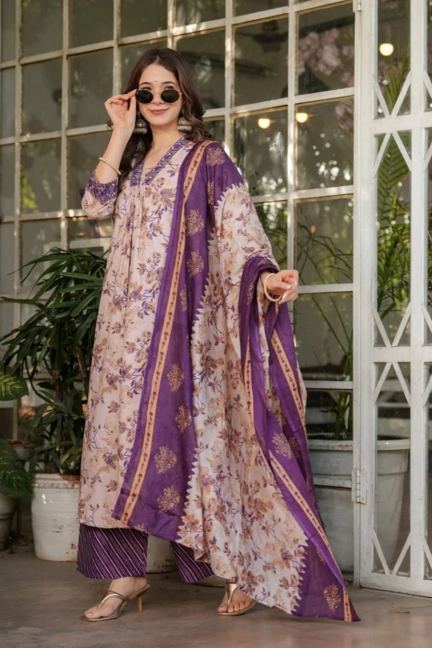 Woman wearing a purple and beige traditional outfit with a floral pattern, standing indoors.