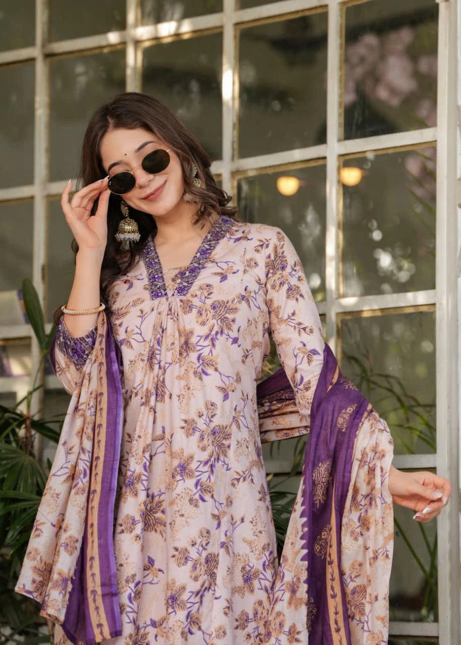 Woman wearing a floral dress with purple accents in front of a window.