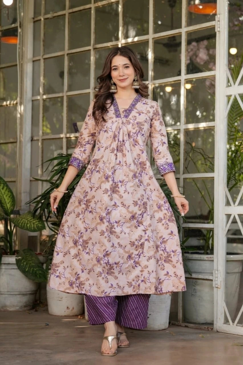 Woman wearing a floral dress with a purple top and pants in an indoor setting with plants.