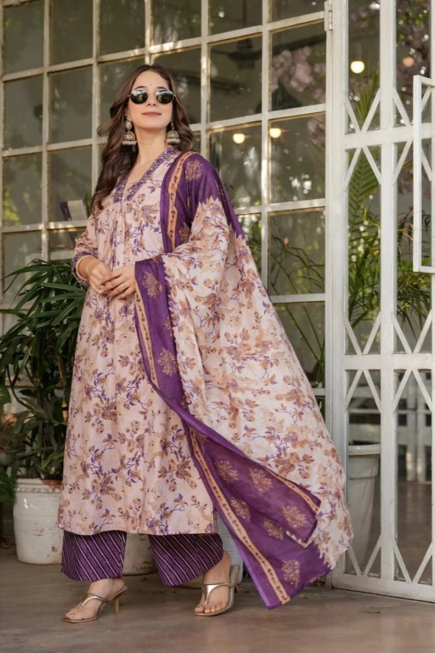 Woman wearing a floral dress with purple accents standing in front of a glass door.