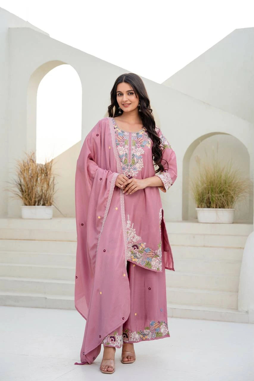 Woman in a pink traditional outfit with floral patterns standing in a white architectural setting.