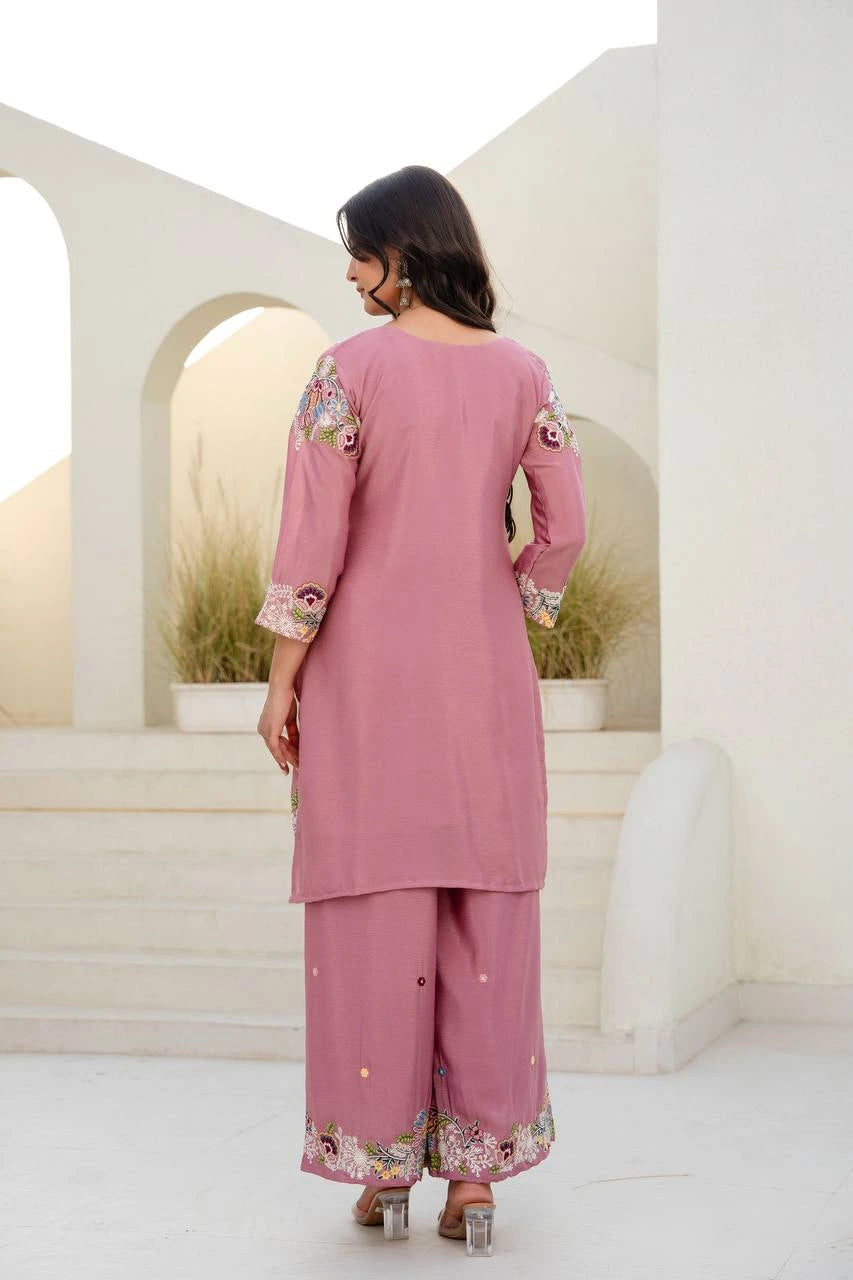 Woman wearing a pink traditional outfit with floral patterns in an outdoor setting.