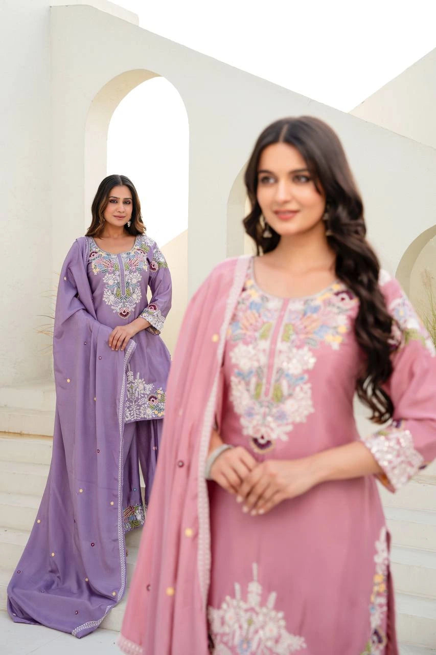 Two women in traditional embroidered dresses standing in a decorative interior setting.