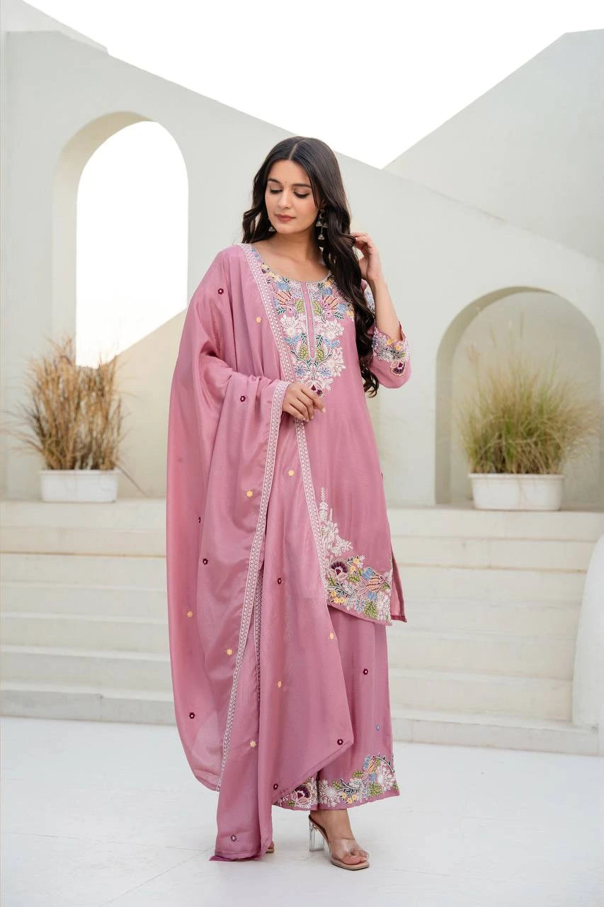 Woman in a pink traditional outfit with floral patterns standing in a white architectural setting.