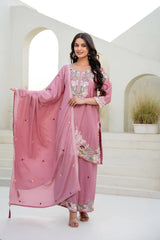 Woman in a pink traditional outfit with floral patterns in an elegant indoor setting.