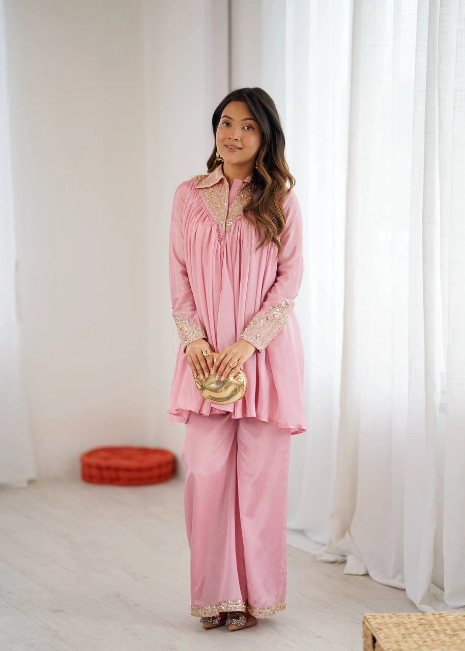 Woman in a pink traditional outfit standing in a room with white curtains.