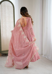 Woman wearing a pink saree with white floral embroidery in a minimal indoor setting.