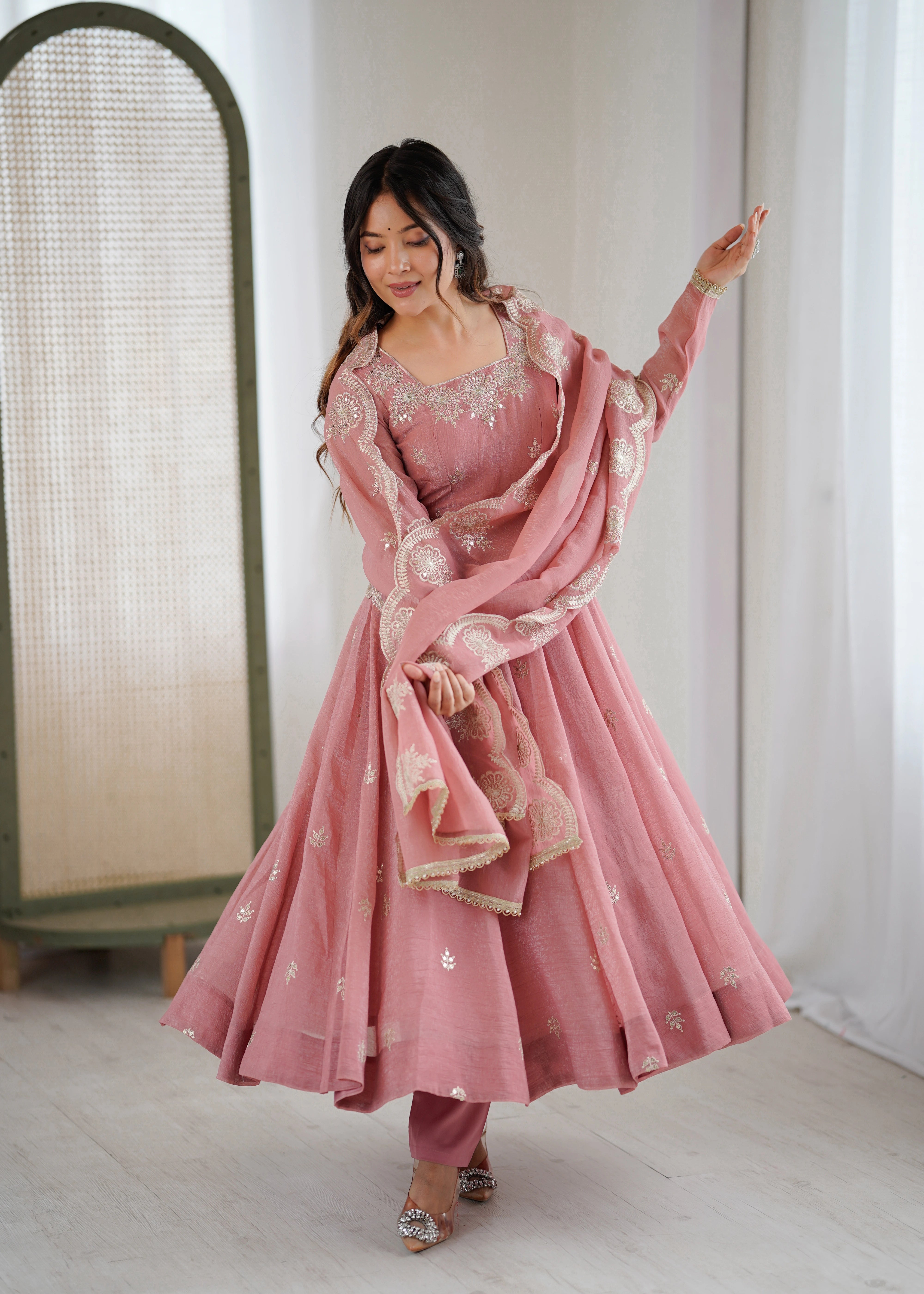 Woman in a pink traditional outfit with a matching dupatta in a minimalistic setting.